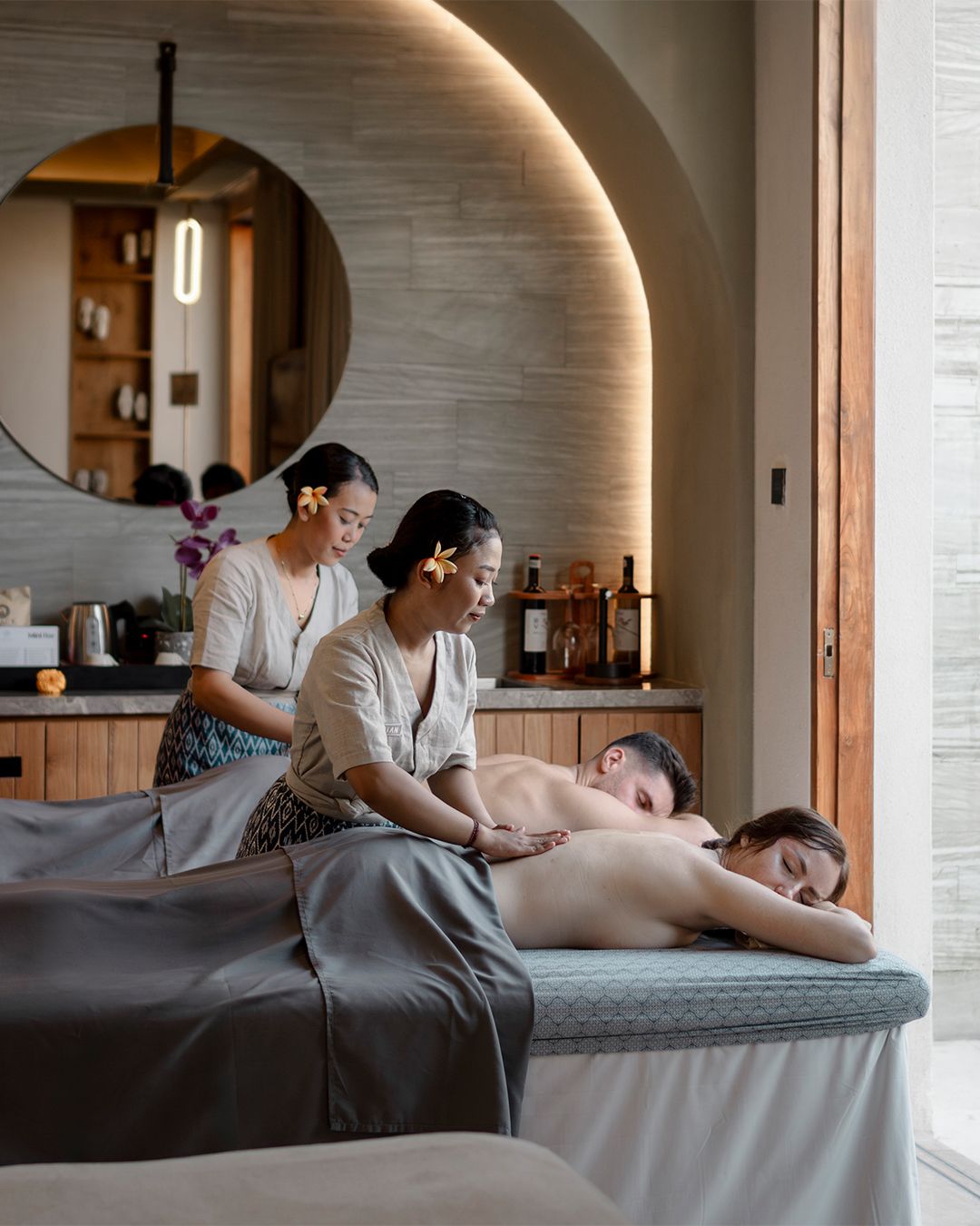 Two certified Thai therapists giving a couples massage on side-by-side tables in a warmly lit villa suite